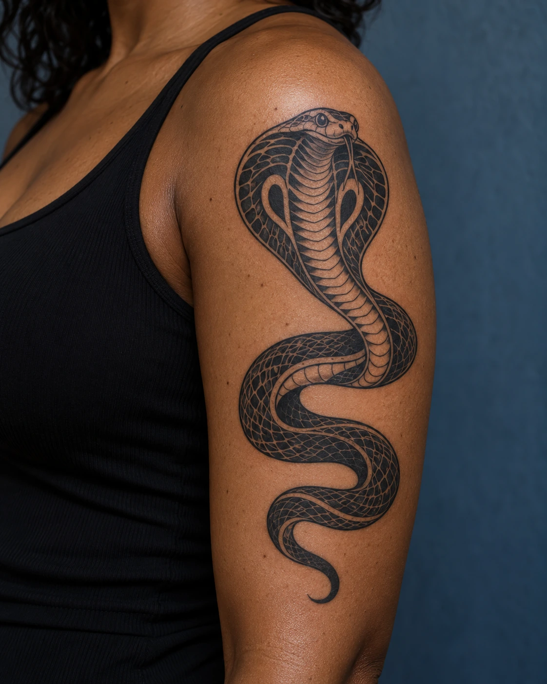 Tatouage serpent : significations, styles et idées pour ton projet | TATOUEZ Cobra noir à coiffe déployée et corps enroulé sur le haut d’un bras à peau brune.