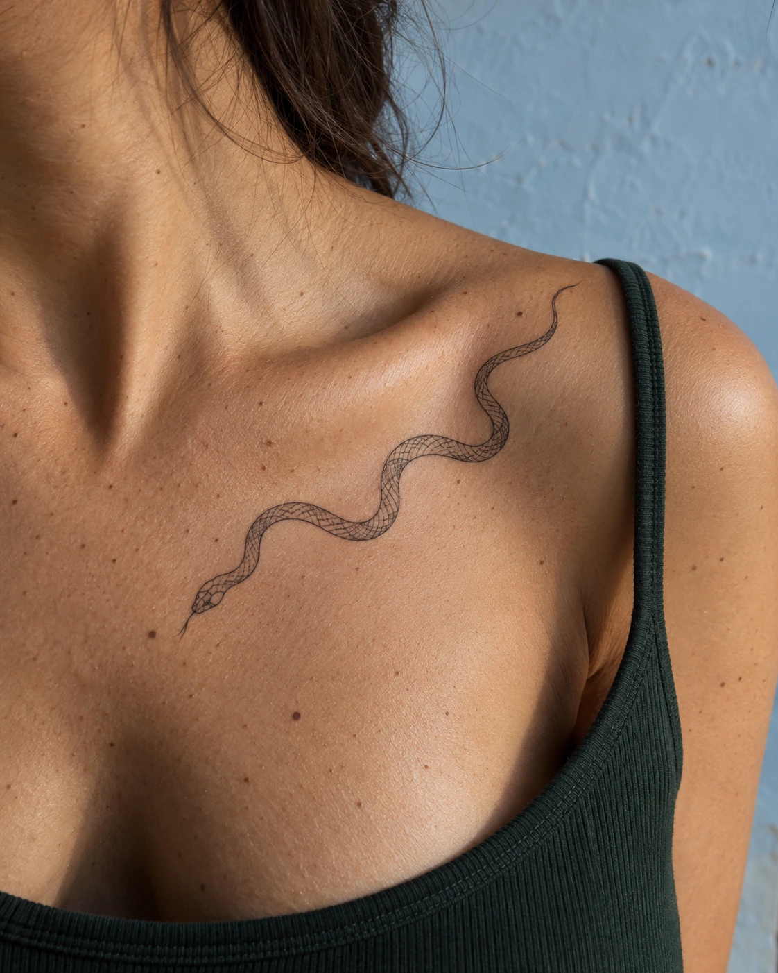 Tatouage serpent : significations, styles et idées pour ton projet | TATOUEZ Serpent noir aux lignes fines suivant une diagonale sous la clavicule, près d’un débardeur vert.